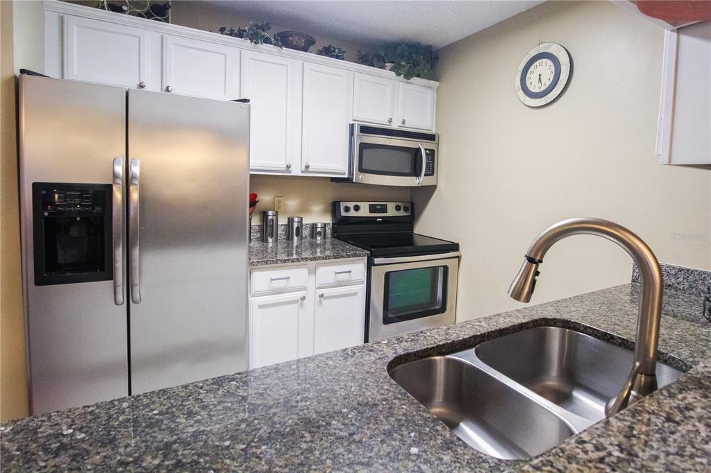 A kitchen features white cabinets, stainless steel appliances, granite countertops, and a double-basin sink — 4009 CROCKERS LAKE BOULEVARD UNIT 11, SARASOTA, FL