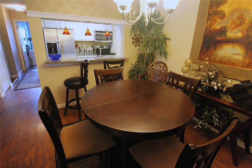 A dining area with a round wooden table, chairs, and a breakfast bar overlooking a kitchen — 4009 CROCKERS LAKE BOULEVARD UNIT 11, SARASOTA, FL