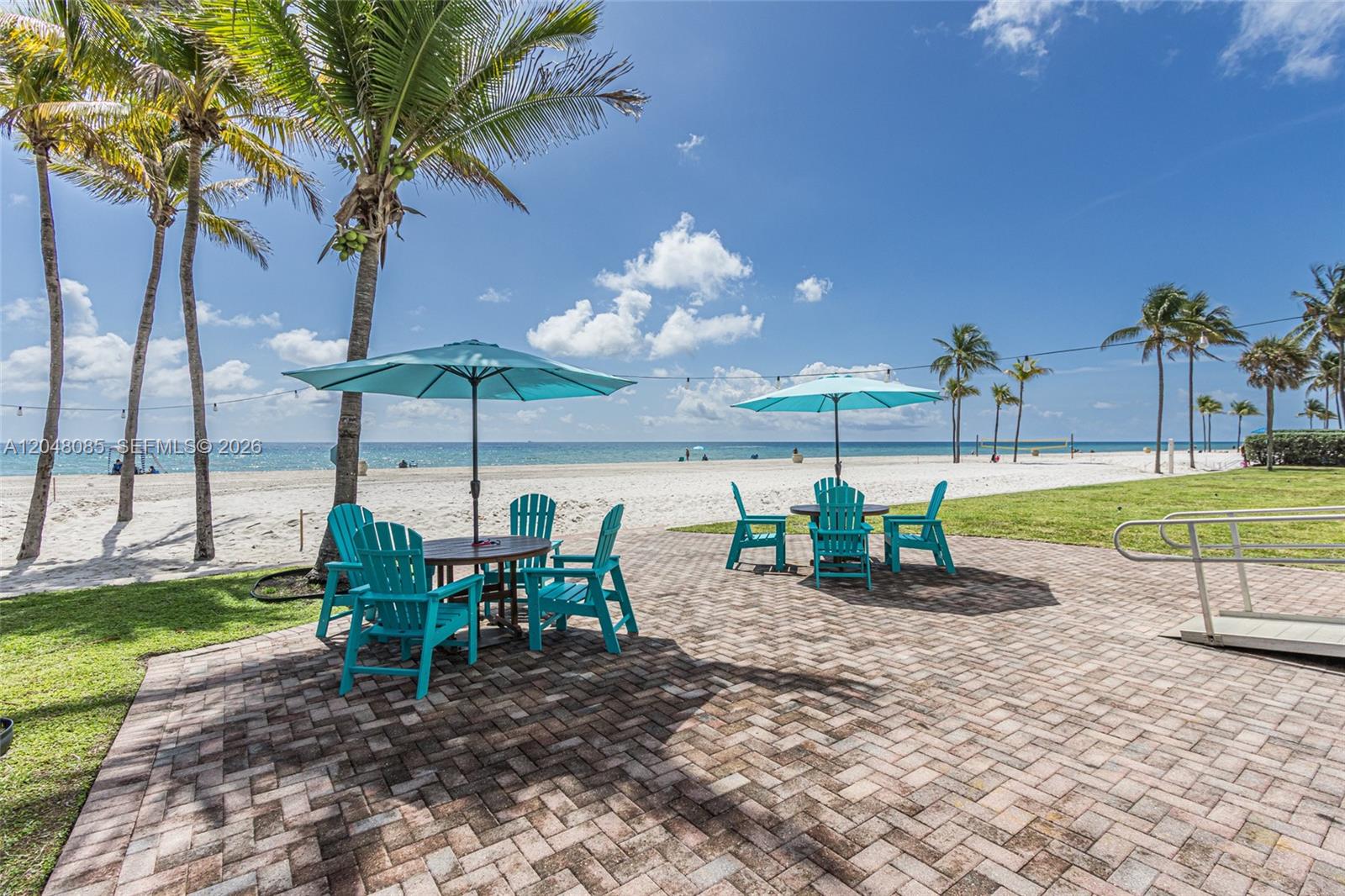 A paved patio features two sets of tables and chairs under umbrellas by the beach — 1801 S Surf Rd # 2G, Hollywood FL 33019, HOLLYWOOD, FL