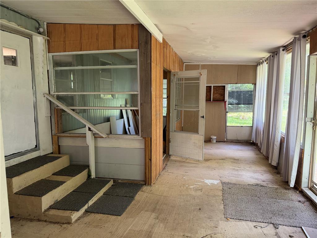 A covered porch features wood-paneled walls, a concrete floor, stairs, and several windows and doors — 196 ROBINHOOD DRIVE, DELAND, FL