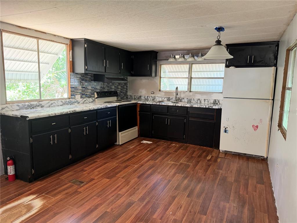 A kitchen features black cabinets, marble-patterned countertops, a white refrigerator, and wood-look flooring — 196 ROBINHOOD DRIVE, DELAND, FL