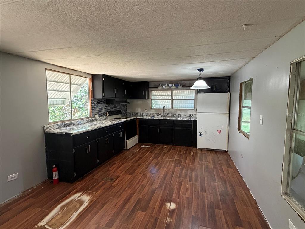 A kitchen features black cabinets, a white refrigerator, and wood-look flooring under a textured ceiling — 196 ROBINHOOD DRIVE, DELAND, FL