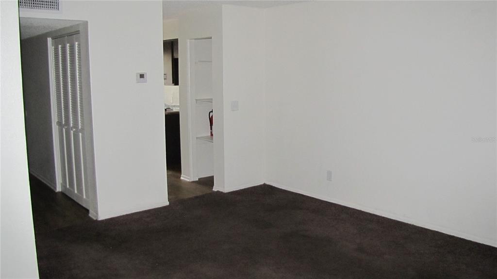 An empty room with dark carpet, white walls, a closet, and a view into a kitchen — 7506 NEEDLE LEAF PLACE UNIT 56, TAMPA, FL