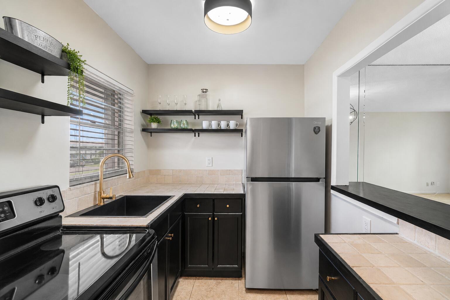 A kitchen features black cabinets, stainless steel appliances, a gold faucet, and open shelving — 1116 Lake Terrace # 207, Boynton Beach FL 33426, BOYNTON BEACH, FL