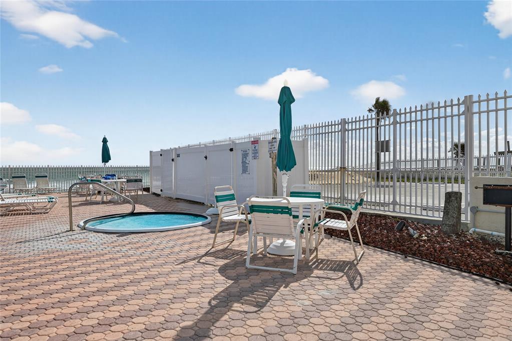 A paved pool deck features a small hot tub, patio furniture, and a white fence — 701 S ATLANTIC AVENUE UNIT 111, DAYTONA BEACH, FL