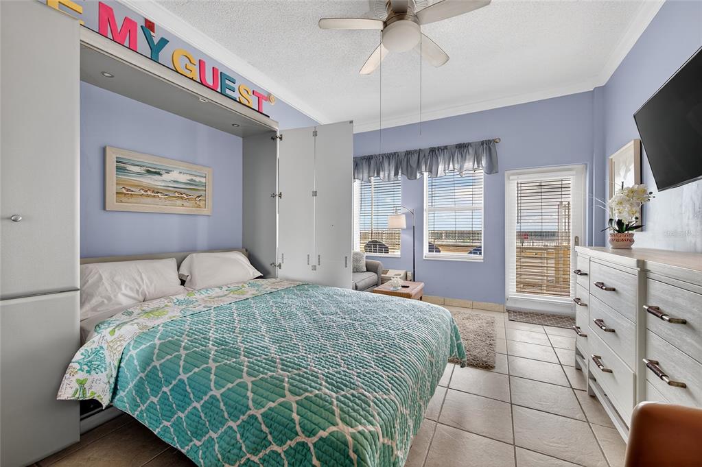 A bedroom features a pull-down bed, light blue walls, tile flooring, and a balcony door — 701 S ATLANTIC AVENUE UNIT 111, DAYTONA BEACH, FL