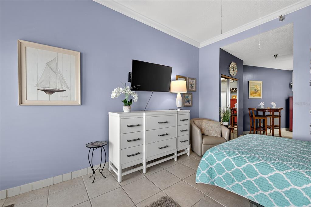 A bedroom features light blue walls, a white dresser with a television, and tile flooring — 701 S ATLANTIC AVENUE UNIT 111, DAYTONA BEACH, FL