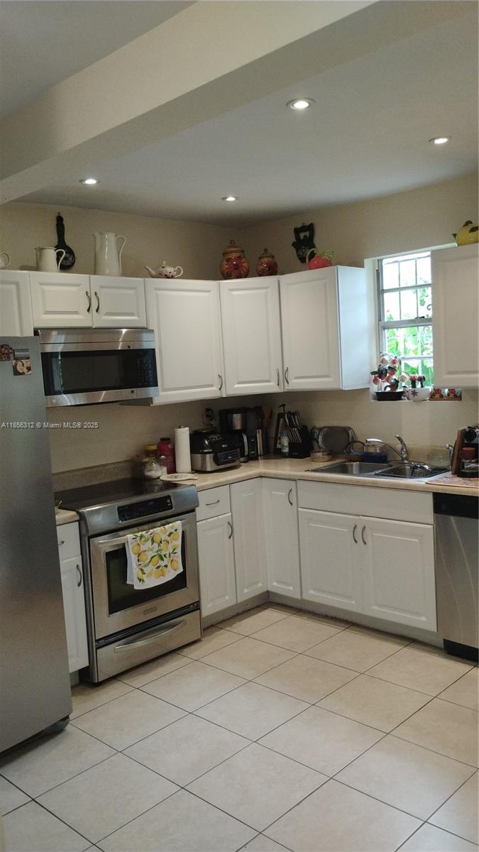 A kitchen features white cabinets, stainless steel appliances, and light-colored tile flooring — 7312 NW 17th Ct, Miami FL 33147, MIAMI, FL