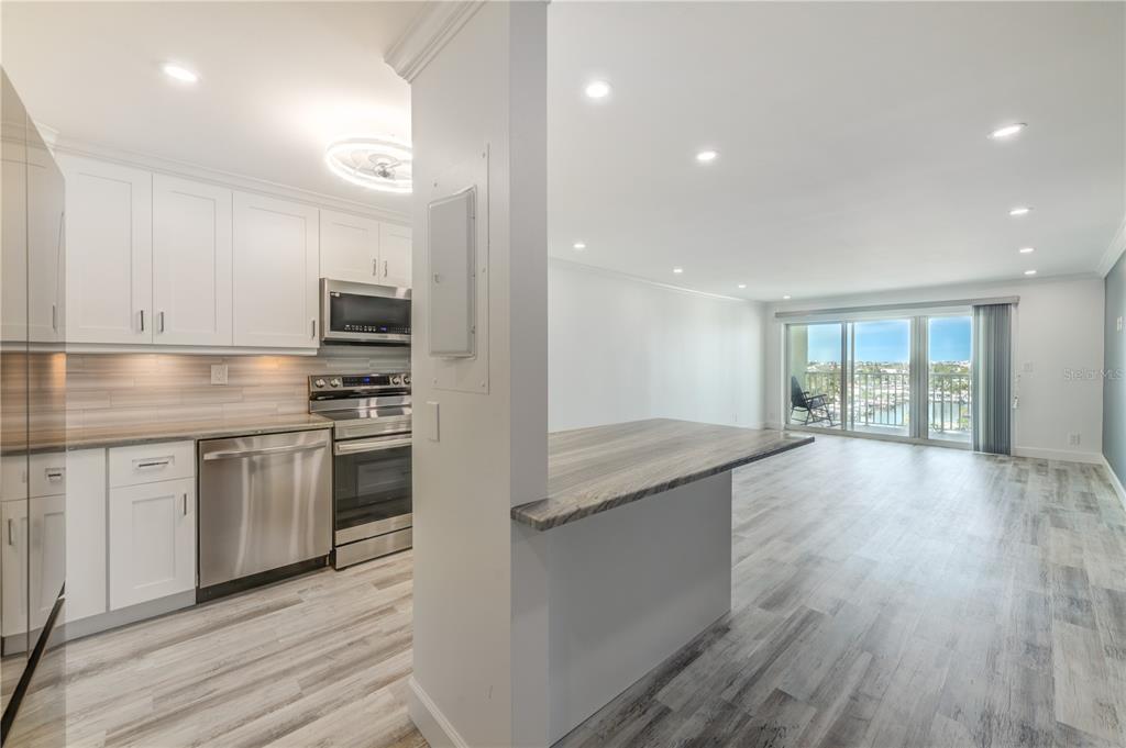 A modern kitchen with white cabinets and stainless steel appliances opens to a living area — 400 64TH AVENUE UNIT 901, ST PETE BEACH, FL