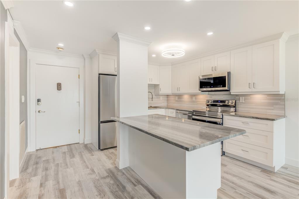 A modern kitchen features white cabinets, stainless steel appliances, and a gray stone-topped island — 400 64TH AVENUE UNIT 901, ST PETE BEACH, FL