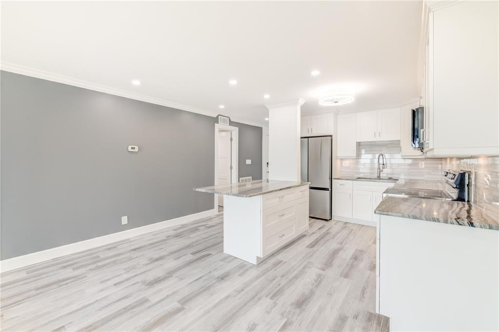 A modern kitchen features white cabinets, granite countertops, a central island, and gray wood flooring — 400 64TH AVENUE UNIT 901, ST PETE BEACH, FL