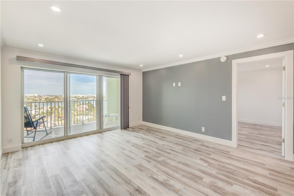 A living room with light wood-look flooring, a gray accent wall, and a sliding glass door — 400 64TH AVENUE UNIT 901, ST PETE BEACH, FL