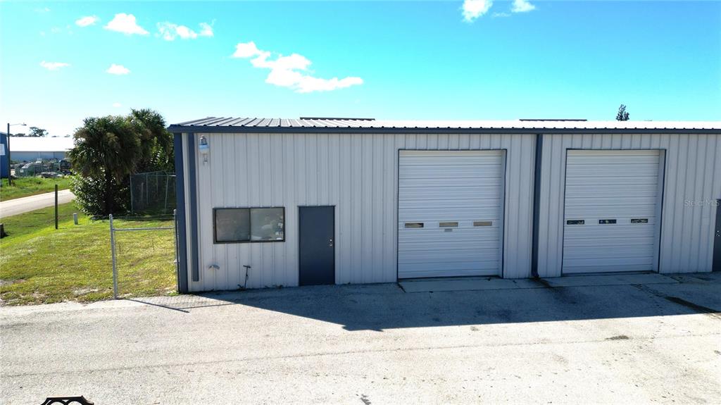 An exterior view of a metal industrial building with two roll-up doors and a side entrance — 5475 WILLIAMSBURG DRIVE, PUNTA GORDA, FL