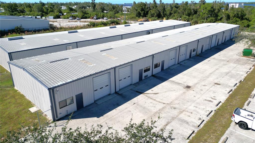 An aerial view shows a long, metal-sided commercial warehouse building with multiple roll-up garage doors — 5475 WILLIAMSBURG DRIVE, PUNTA GORDA, FL