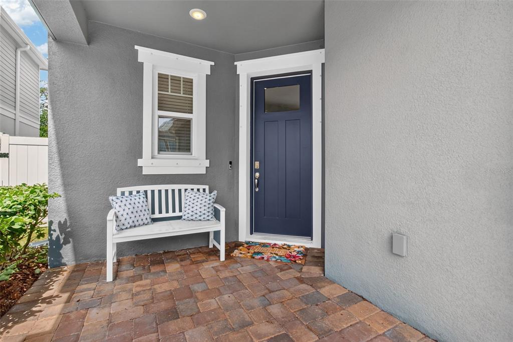 A gray exterior entryway features a blue front door, a white bench, and paver flooring — 8114 ARTISAN CIRCLE, SEMINOLE, FL