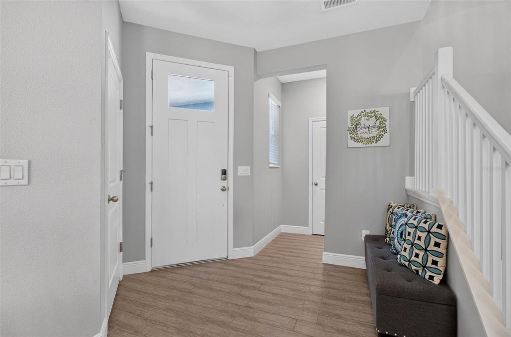 An entryway features light gray walls, wood-look flooring, a white front door, and a bench — 8114 ARTISAN CIRCLE, SEMINOLE, FL