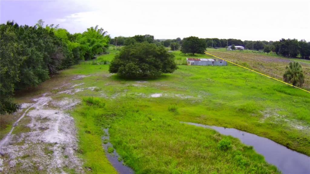 An aerial view shows a grassy field with a small shed, trees, and a stream — 5187 DEER RUN DRIVE, ZOLFO SPRINGS, FL