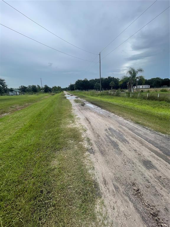 A dirt road with puddles runs through a grassy field under a cloudy sky — 5187 DEER RUN DRIVE, ZOLFO SPRINGS, FL