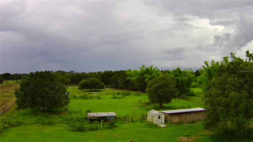 An aerial view of a grassy field with trees, a small shed, and outbuildings — 5187 DEER RUN DRIVE, ZOLFO SPRINGS, FL