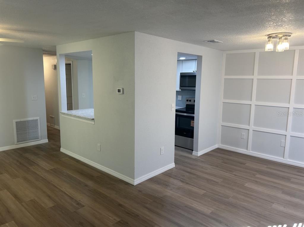 A view of a living area with wood-look flooring, a kitchen pass-through, and paneled walls — 121 LOBLOLLY COURT UNIT C, OLDSMAR, FL