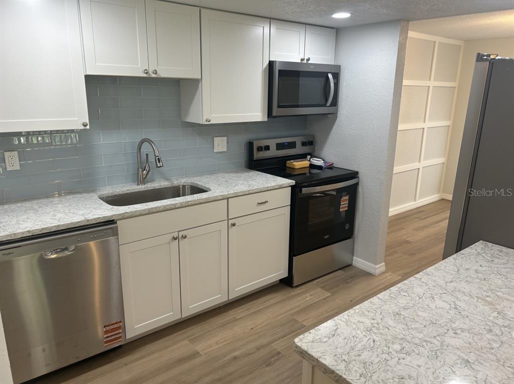 A kitchen features white cabinets, stainless steel appliances, light countertops, and a blue backsplash — 121 LOBLOLLY COURT UNIT C, OLDSMAR, FL