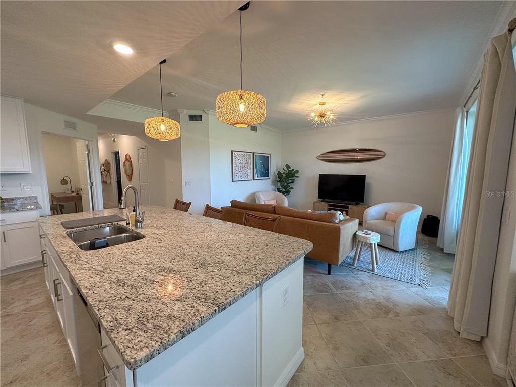 A kitchen island with granite countertops overlooks an open-concept living room with a sofa — 14040 HERITAGE LANDING BOULEVARD UNIT 113, PUNTA GORDA, FL