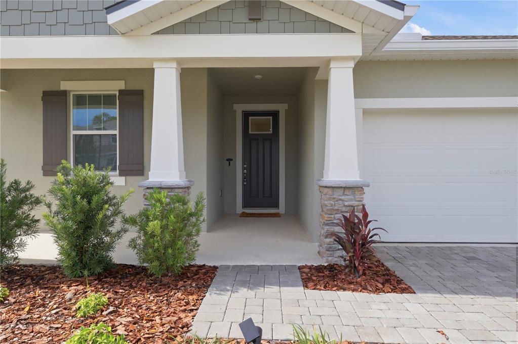 The exterior of a house features a covered entryway with stone-based columns and a dark door — 1733 CARNELIAN STREET, DELAND, FL