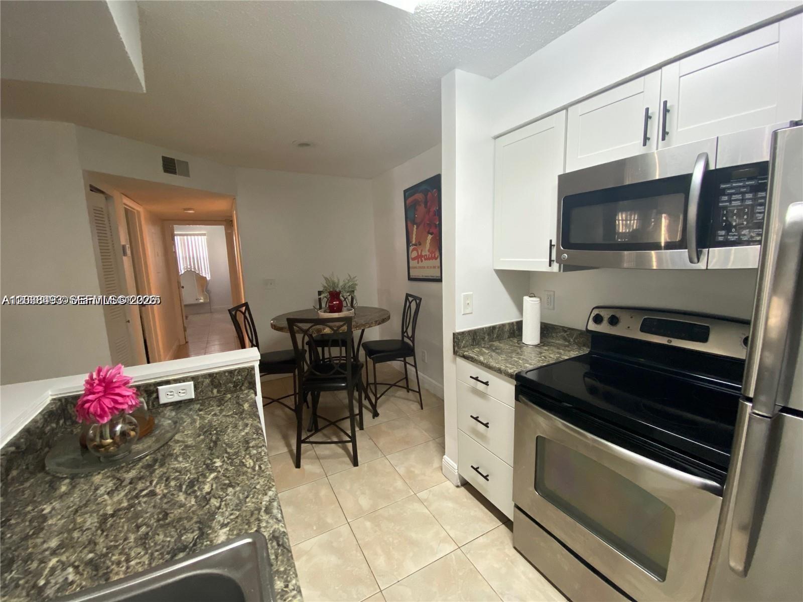 A kitchen with white cabinets, stainless steel appliances, and a small dining area — 1257 SW 46th Ave # 1801, Pompano Beach FL 33069, POMPANO BEACH, FL