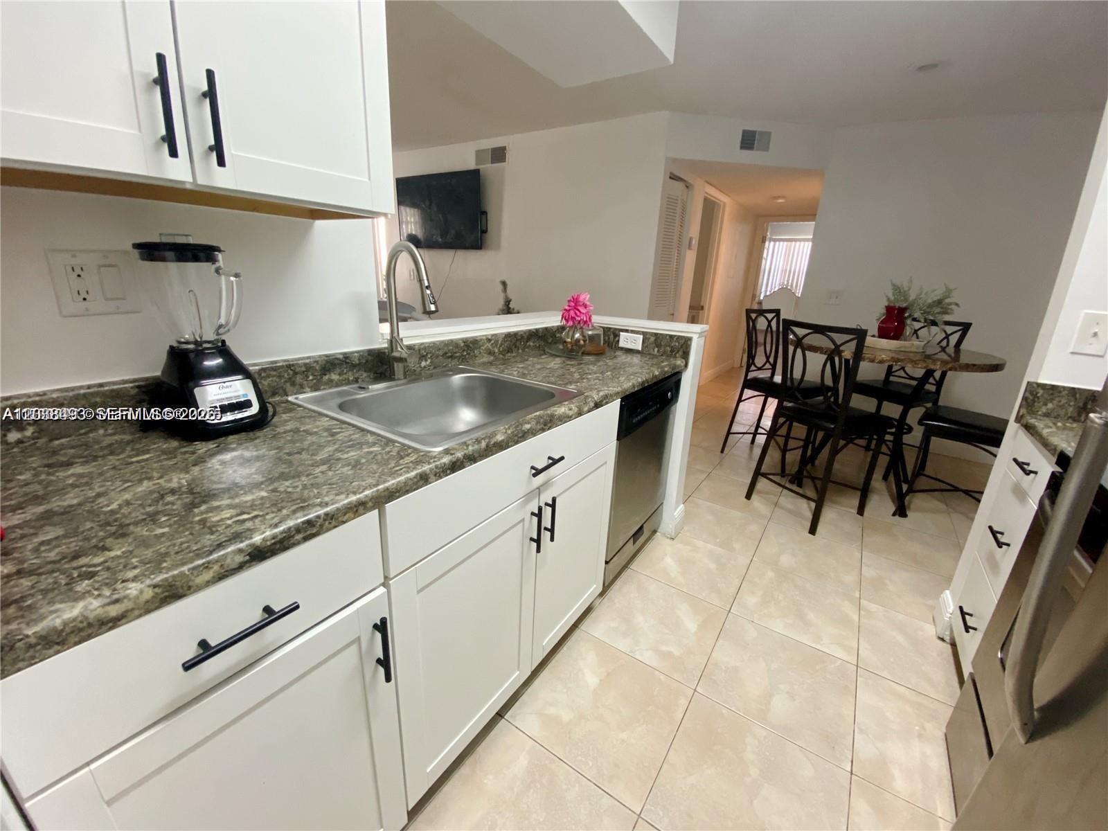 A kitchen features white cabinets, dark countertops, a stainless steel sink, and a dining area — 1257 SW 46th Ave # 1801, Pompano Beach FL 33069, POMPANO BEACH, FL