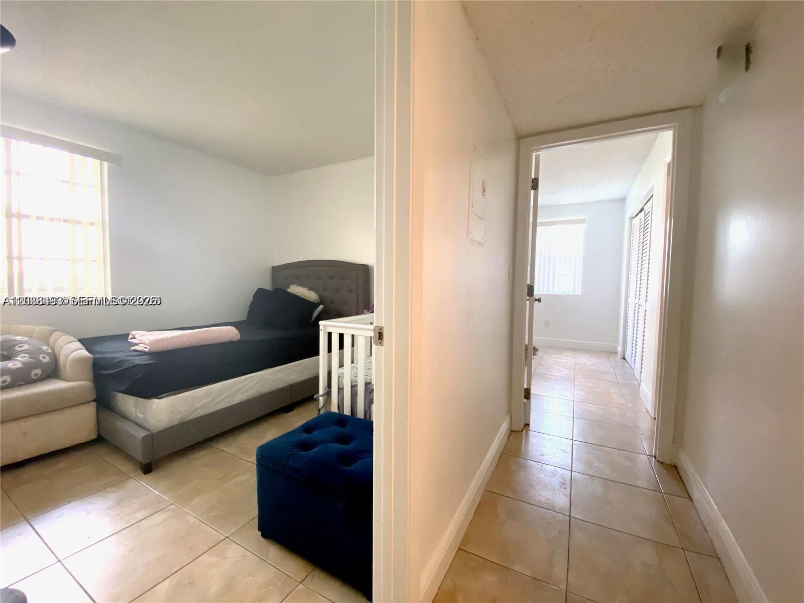A bedroom with a bed and crib connects to a hallway with tiled floors — 1257 SW 46th Ave # 1801, Pompano Beach FL 33069, POMPANO BEACH, FL