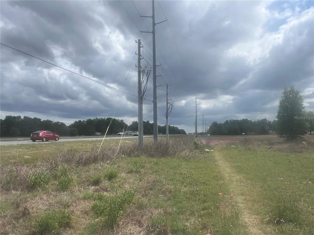 A grassy field with utility poles runs alongside a road with a red car — 00 S US HWY 301, SUMMERFIELD, FL