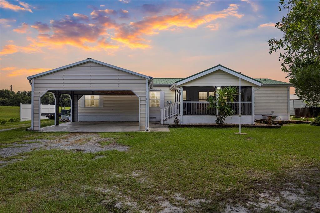 A single-story house with a carport and a screened-in porch under a sunset sky — 8945 SE 57TH DRIVE, OKEECHOBEE, FL