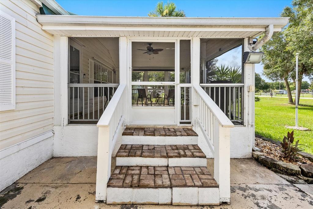 A screened-in porch with brick steps leads to a white door on a house exterior — 8945 SE 57TH DRIVE, OKEECHOBEE, FL