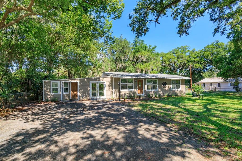 A single-story house with tan siding and a gravel driveway sits under large oak trees — 2820 MAGNOLIA AVENUE, SANFORD, FL