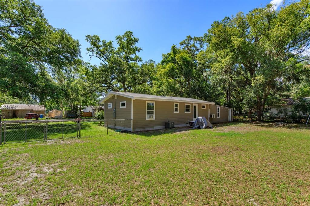 A tan mobile home sits on a grassy lot surrounded by mature trees and fencing — 2820 MAGNOLIA AVENUE, SANFORD, FL