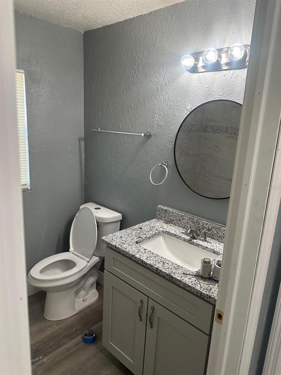 A small bathroom features a gray vanity with a granite countertop, toilet, and round mirror — 724 GROVE AVENUE, ORLANDO, FL