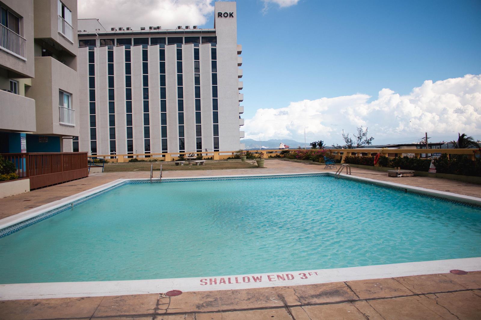A rectangular swimming pool sits on a patio in front of a tall hotel building — 8 Ocean Blvd Kingston Jamaica Boulevard, FL