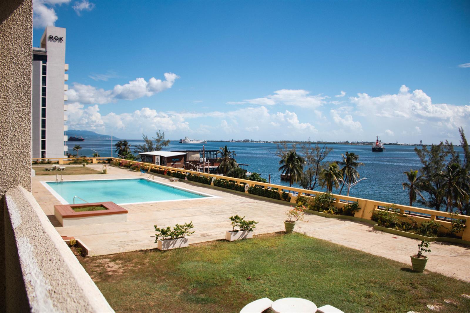 An elevated view of a hotel pool deck overlooking a harbor with ships and palm trees — 8 Ocean Blvd Kingston Jamaica Boulevard, FL