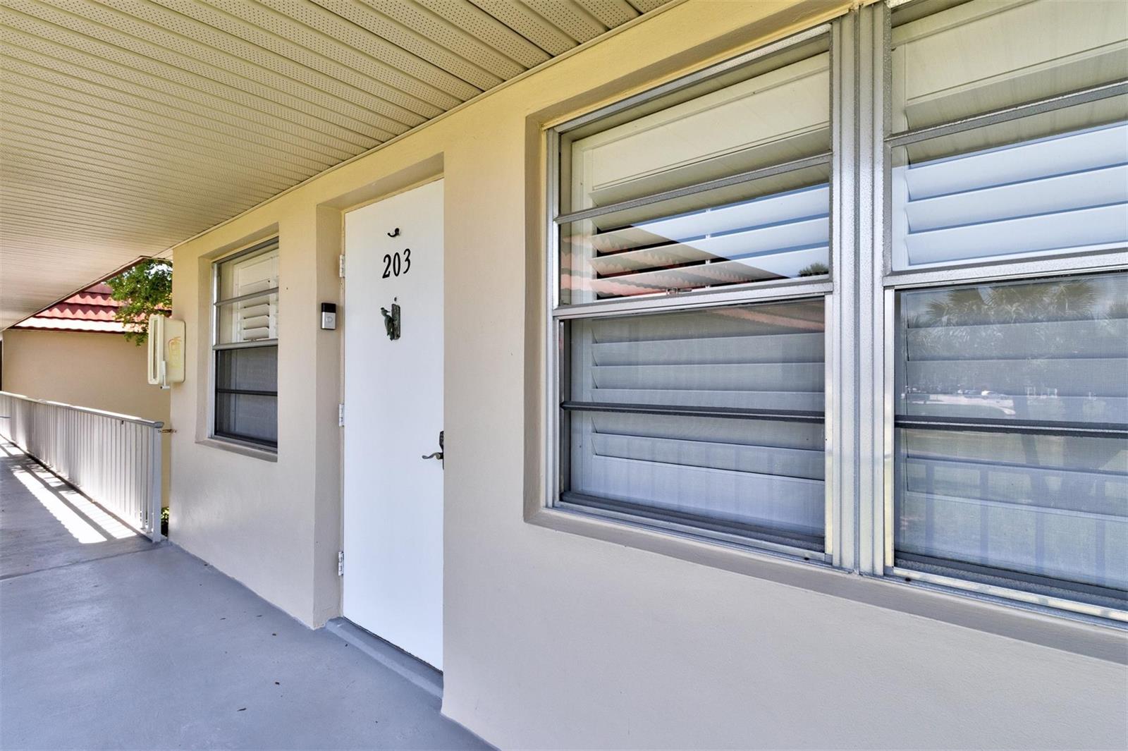 An exterior view of an apartment building walkway featuring a white door numbered 203 — 63 Woodland Drive, Vero Beach FL 32962, VERO BEACH, FL