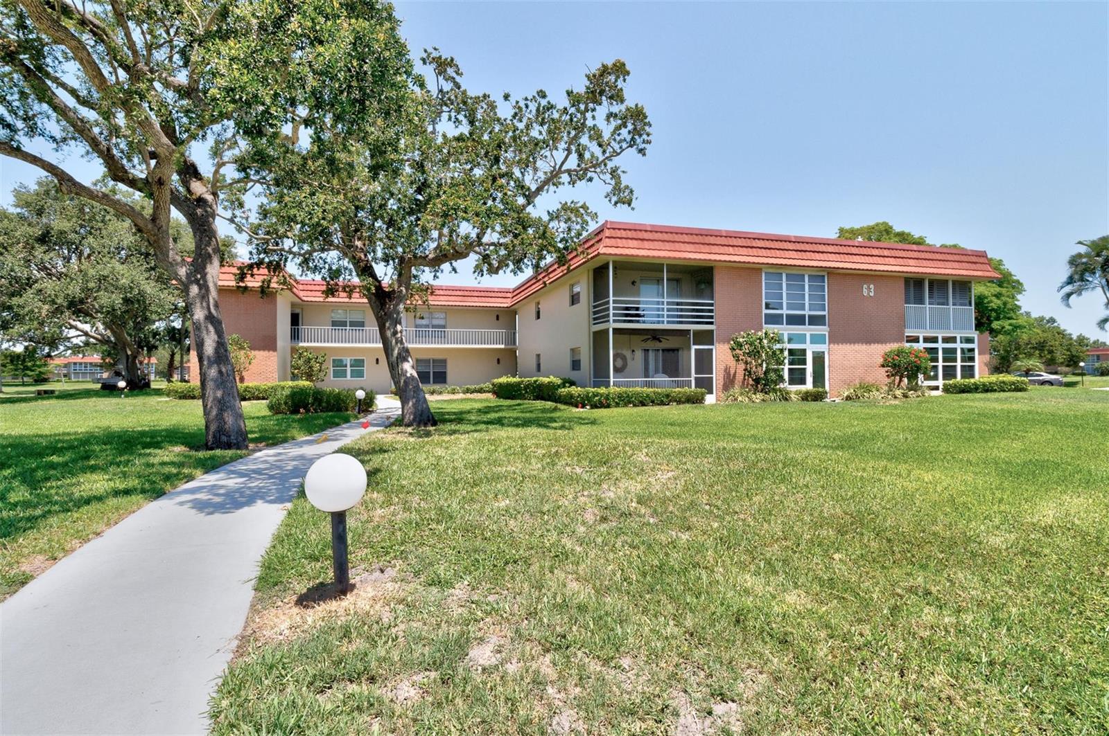 A two-story brick apartment building with a red tile roof sits behind a grassy lawn — 63 Woodland Drive, Vero Beach FL 32962, VERO BEACH, FL