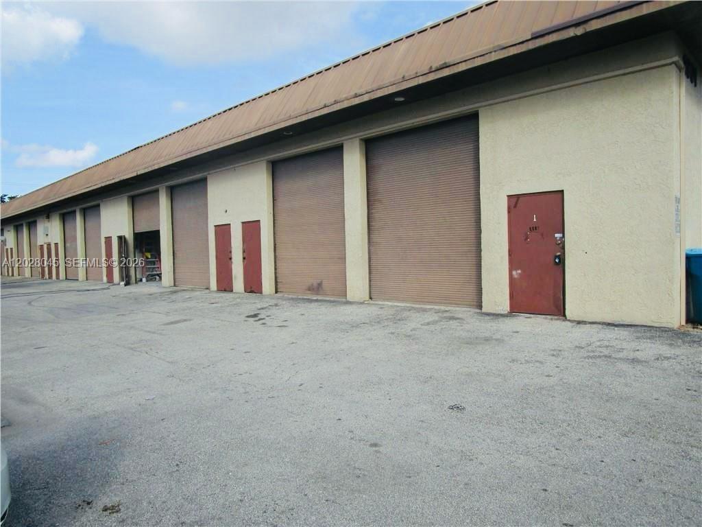 An exterior view of a commercial warehouse building featuring multiple roll-up doors and a pedestrian entrance — 1901 NW 32nd St # 6, Pompano Beach FL 33064, POMPANO BEACH, FL