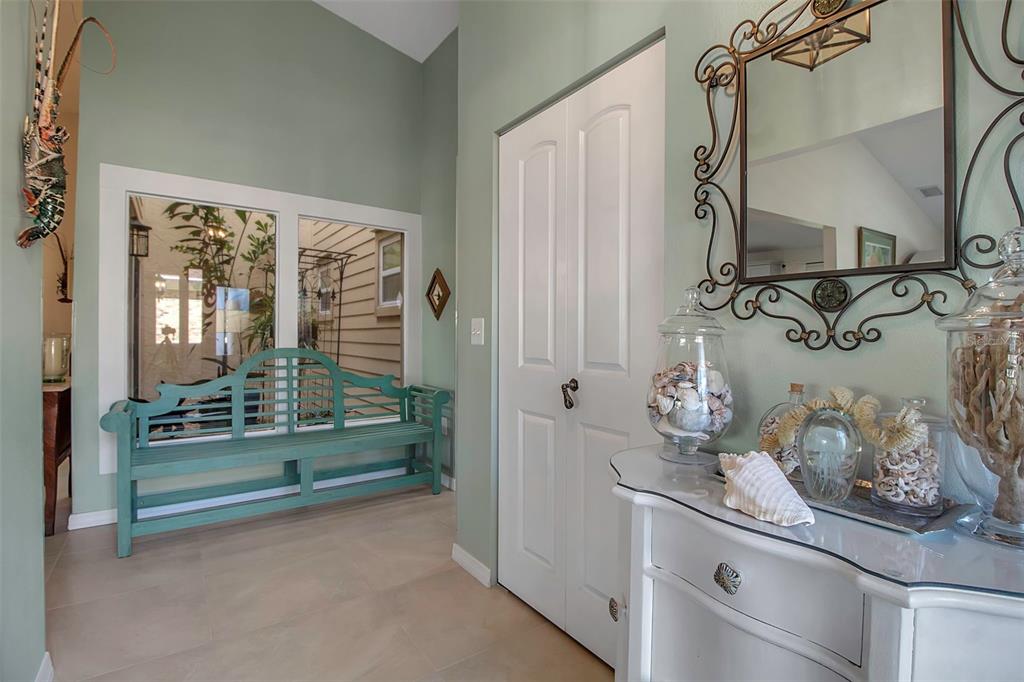 A bright entryway features a light green bench, a white console table, and a mirror — 3410 AVENIDA MADERA UNIT B, BRADENTON, FL