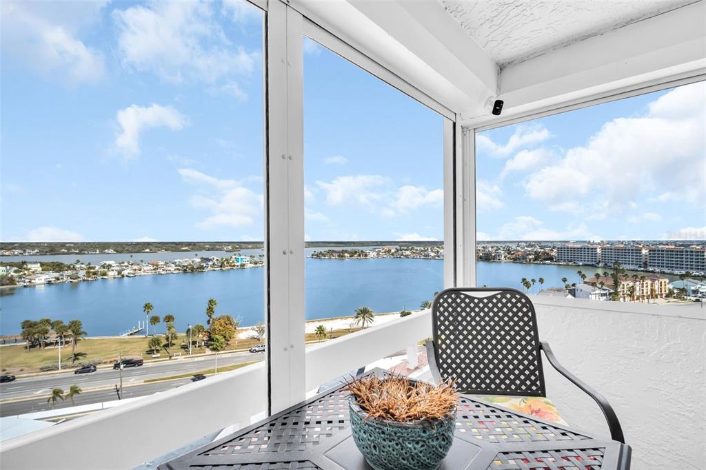 A screened-in balcony overlooks a bay with a road, palm trees, and distant buildings — 17900 GULF BOULEVARD UNIT 12A, REDINGTON SHORES, FL