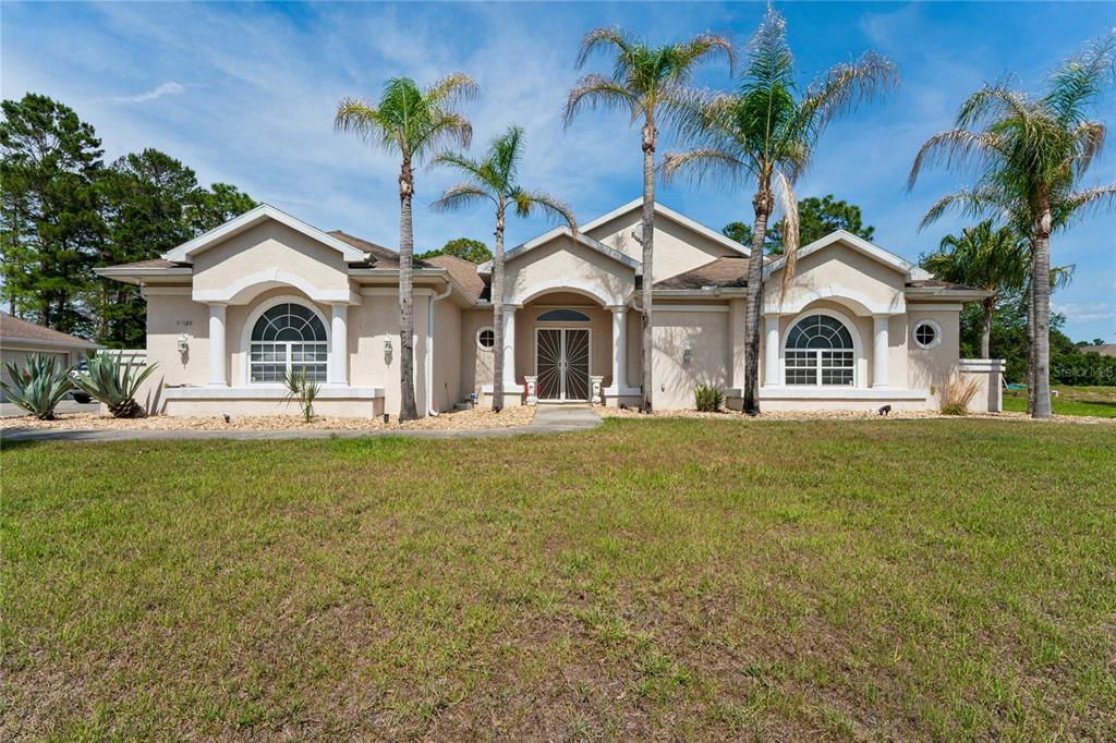 A single-story beige stucco house with a tiled roof, arched windows, and several palm trees — 10120 SHORTLEAF COURT, WEEKI WACHEE, FL