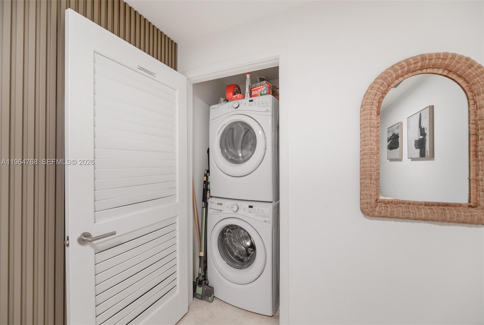 A white laundry closet contains a stacked washer and dryer next to a wicker-framed mirror — 88 SW 7th St # 2204, Miami FL 33130, MIAMI, FL