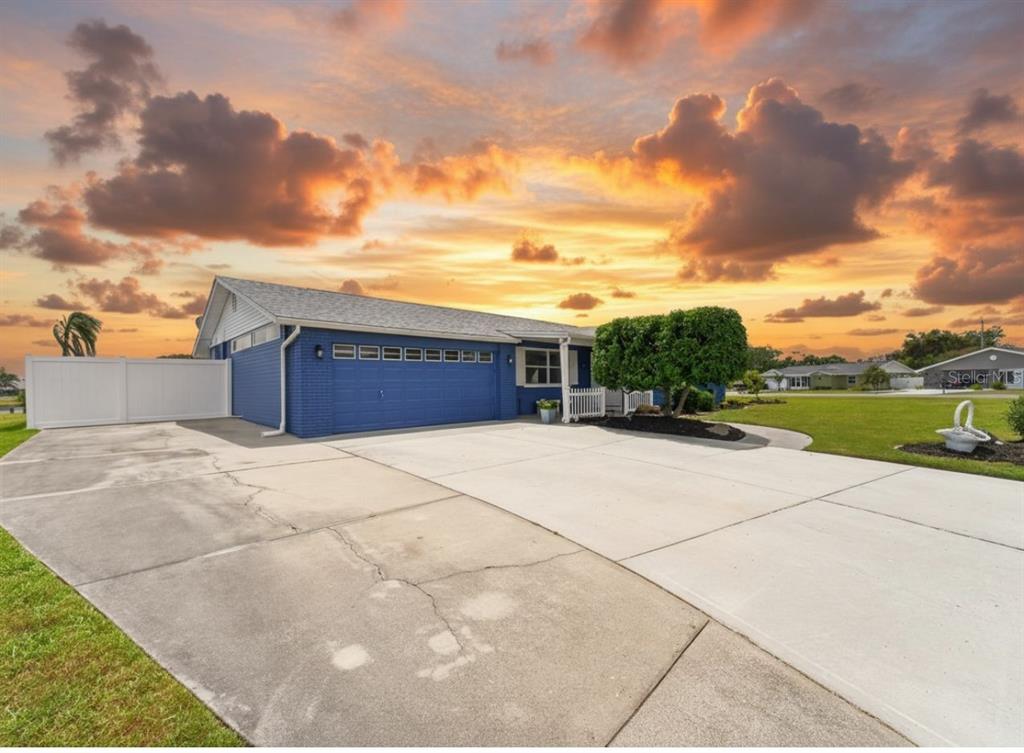 A blue brick house with a large concrete driveway under a vibrant sunset sky — 1810 MILFORD CIRCLE, SUN CITY CENTER, FL