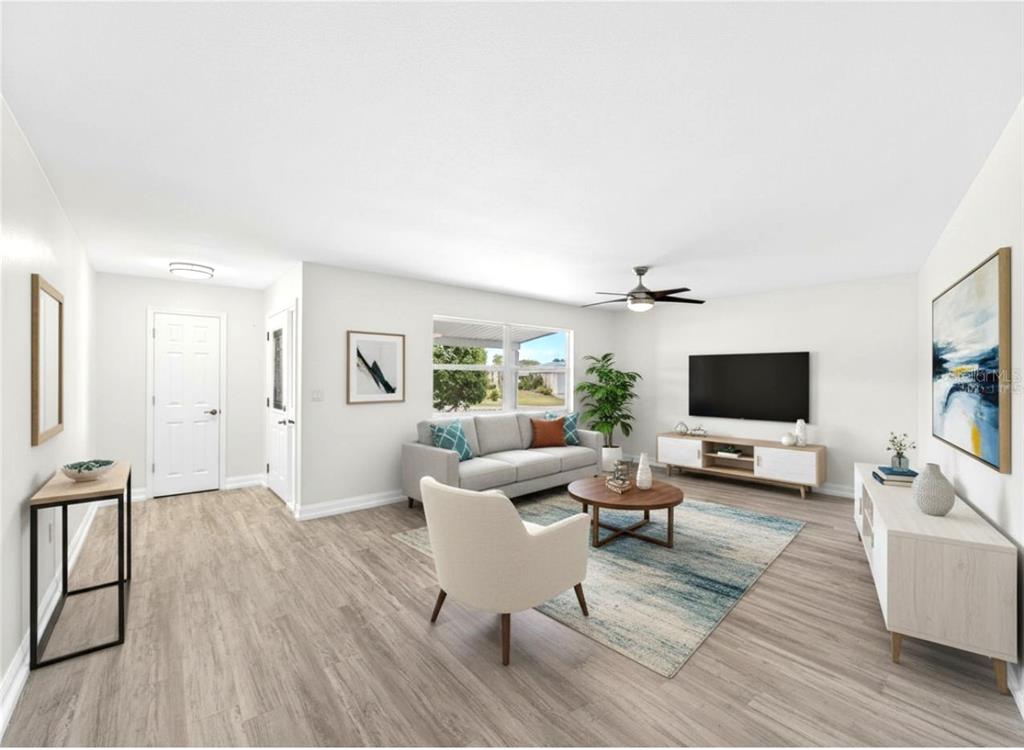A living room with light wood-look flooring, a gray sofa, and a wall-mounted television — 1810 MILFORD CIRCLE, SUN CITY CENTER, FL