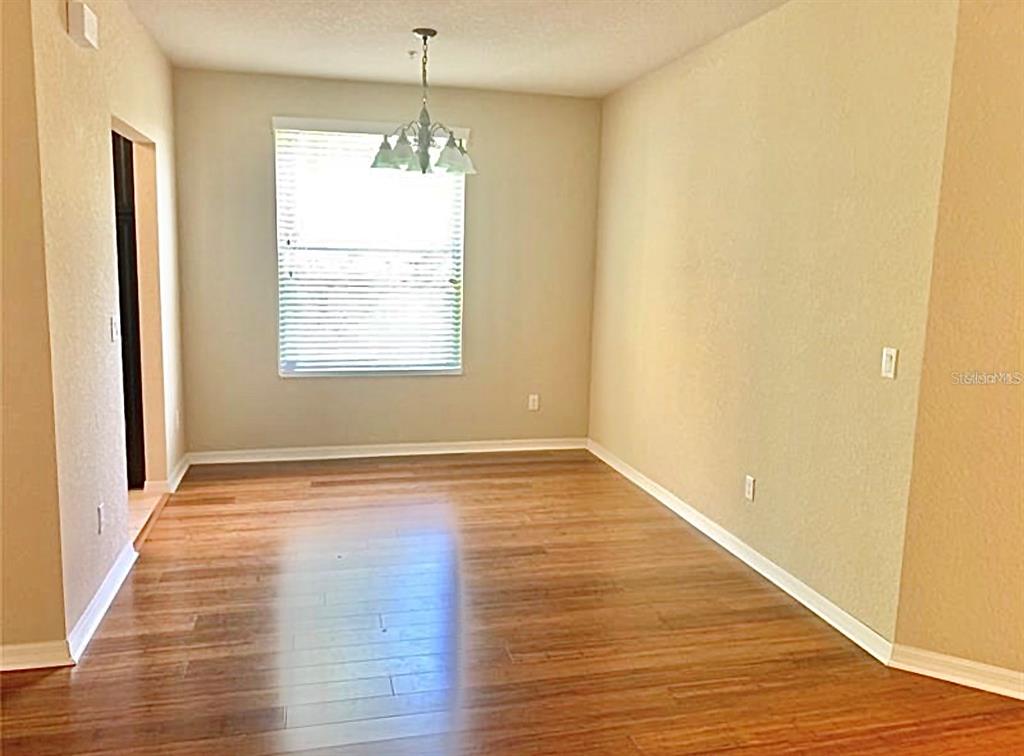 An empty dining room features light-colored walls, wood flooring, and a hanging light fixture — 8363 BELLA TIERRA CT, DAVENPORT, FL