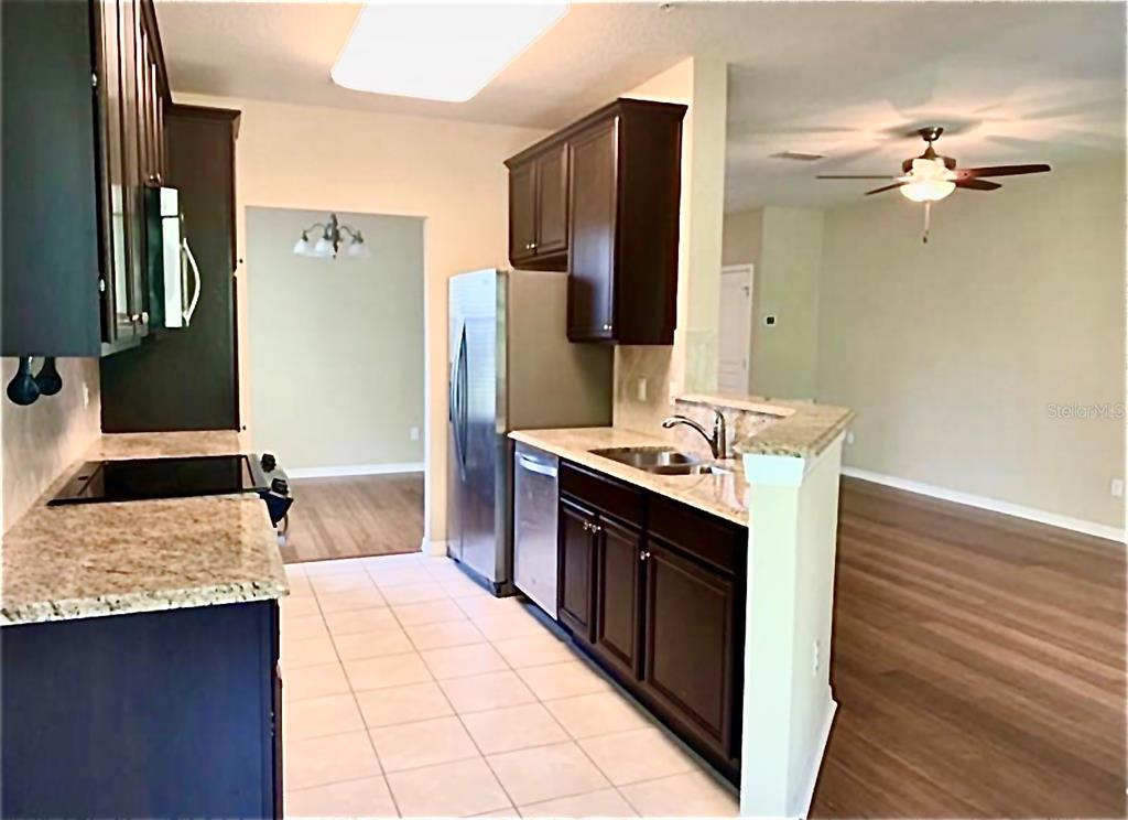 A kitchen with dark wood cabinets, granite countertops, and stainless steel appliances — 8363 BELLA TIERRA CT, DAVENPORT, FL