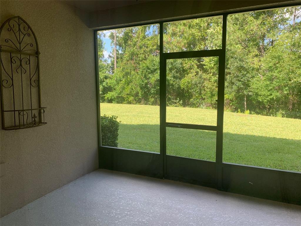 A screened-in patio with a concrete floor and a metal wall decoration overlooking a yard — 8363 BELLA TIERRA CT, DAVENPORT, FL